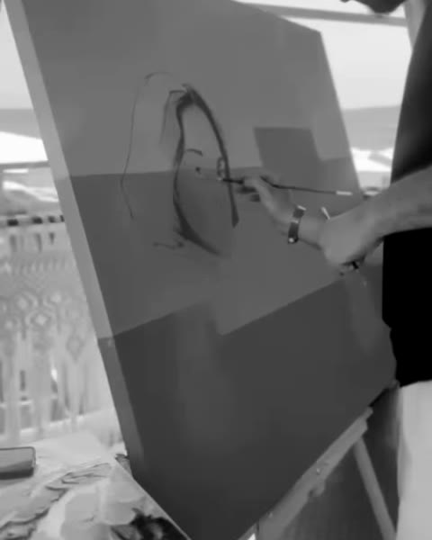 Fırat Koç drawing the outline of a portrait on a grey-green canvas.